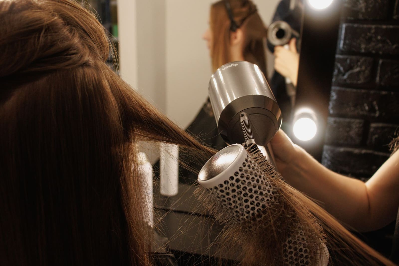 Escova modeladora finalizando o alisamento em cabelo castanho, com secador profissional