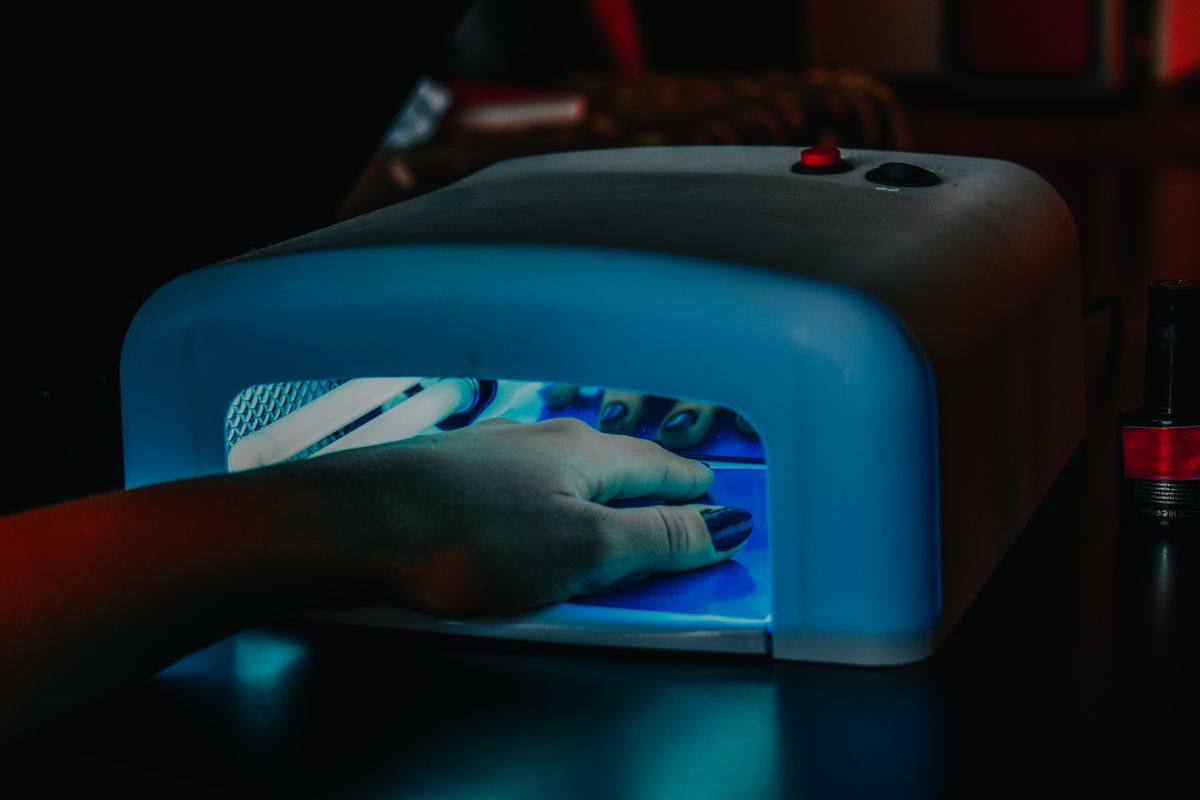Manicure aplicando esmaltação em gel com cabine de luz UV